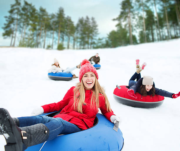 group of happy friends sliding down on snow tubes winter, leisure, sport, friendship and people concept - group of happy friends sliding down on snow tubes sliding down stock pictures, royalty-free photos & images