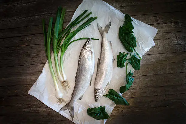 Raw foods - European whitefish (Coregonus lavaretus) with fresh green onions and spinach leaves.
