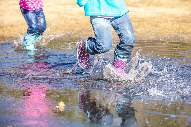 istock Two Young Girls Splashing Through Large Spring Puddle 469902830
