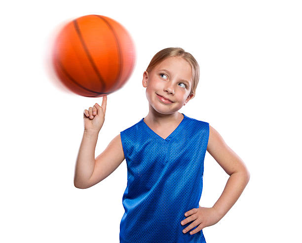 Young elementary age female student spinning a basketball on her finger.  The caucasian blond female is wearing a blue basketball jersey on a white background allowing for copy space.  Please see my portfolio for other images of this model.  
