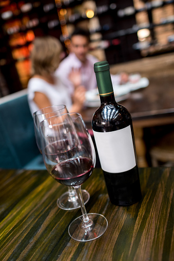 Couple at a restaurant drinking a bottle of red wine - focus on foreground