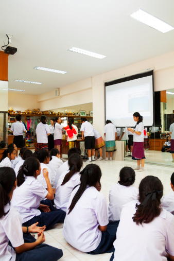 Bangkok, Thailand - February, 6th 2014: Scene in classroom of Satri Wittaya 2 School. Students are sitting on floor and are listening presentation done by some students standing in background. Students are wearing school uniform.