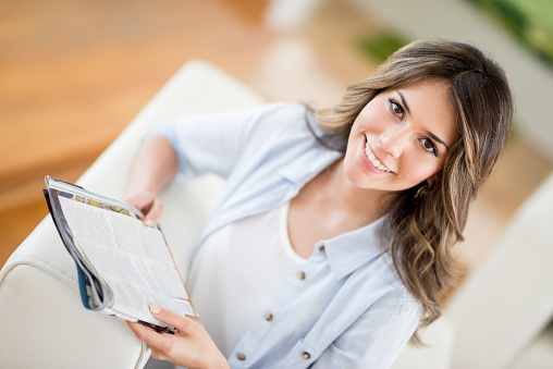 Happy woman reading a magazine at home lying on the sofa