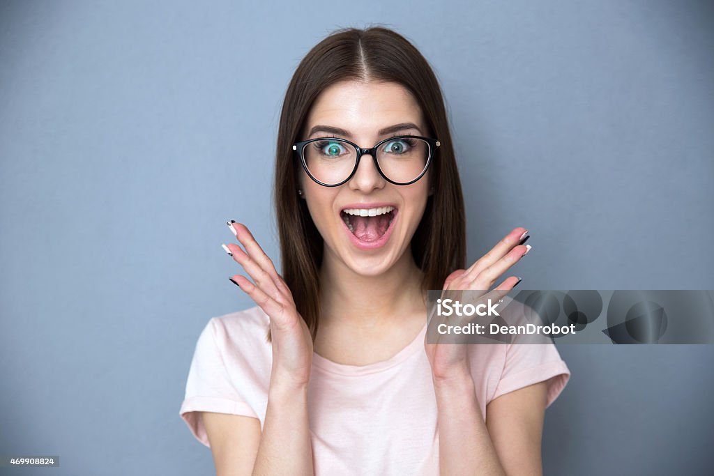 Surprised young woman in glasses Surprised young woman in glasses over gray background Surprise Stock Photo