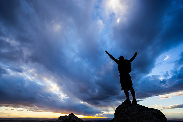 istock silhouette man with arms raised into sunset sky landscape 469909899