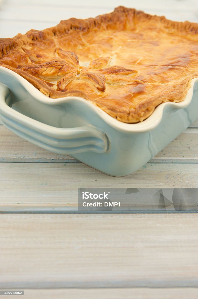 Steak and Ale Pie with Puff Pastry on rustic table An angled view of a homemade traditional British Steak and Ale Pie with a glazed puff pastry top decorated with Pastry leaves. The Pie is in a pale blue ceramic serving dish and rests on a rustic distressed wooden table top. There is plenty of room for copy- space below the pie. 2015 Stock Photo