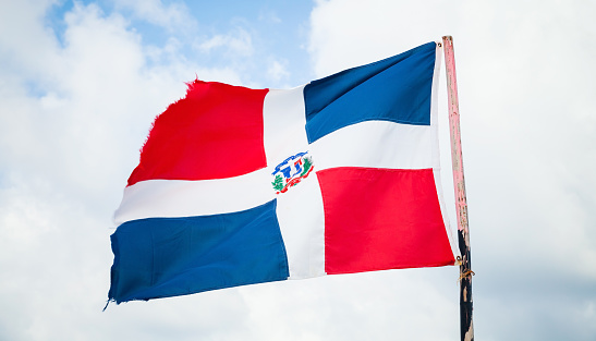 Flag of Dominican republic is waving on wind over cloudy sky background