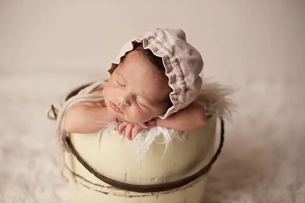 A newborn girl sleeping in an antique bucket.