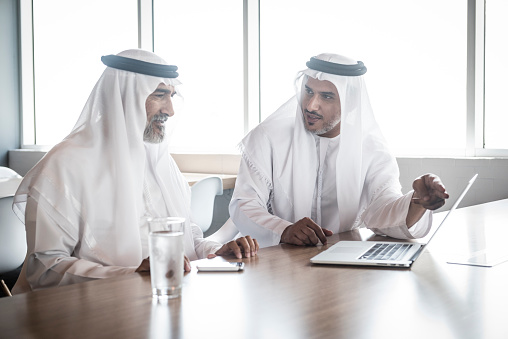Candid portrait of two Emirati arab businessman in discussion at business meeting. They are wearing traditional ghtr