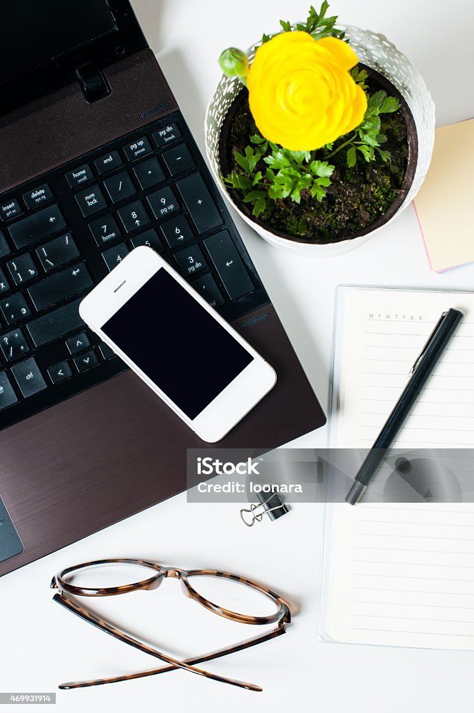 Desktop, home office Desktop, home office: a laptop, notebooks, glasses, smart phone, flower, pens and pencils on a white background 2015 Stock Photo