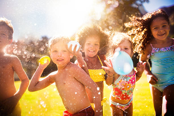 mezclada raza grupo de niños tirando water balloons at camera - outdoor toy fotografías e imágenes de stock