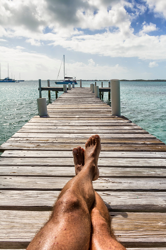 Man Lying on jetty at sunset. In background some sailing boats - Bahamas - Exuma 