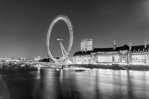 Londen, United Kingdom - November 29, 2013: London skyline at night with the Edf Energy London Eye, the Aquarium and the Hungerford bridge with lights reflecting int the Thames. Long exposure shot in black & white.