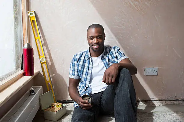 A happy repairman smiles at the camera while sitting eating his lunch taking a break from decorating.