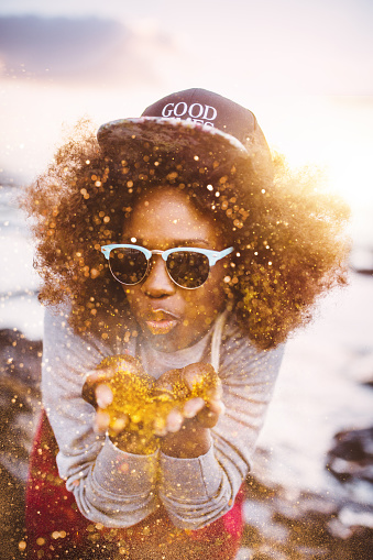 Teen Afro hipster girl bending over and blowing gold glitter happily from her hands