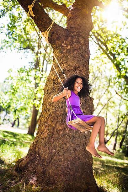 istock Happy Afro girl swinging under a sunlit tree 469937322