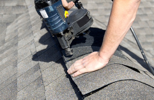 handyman using nail gun to install shingle to repair roof