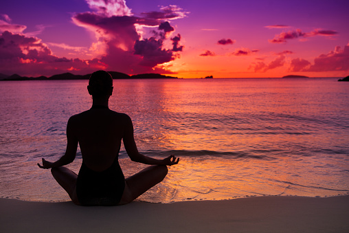 unrecognizable woman meditating in lotus pose at sunset on a beach in St.John, US Virgin Islands