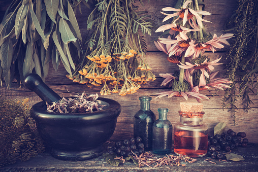 Vintage stylized photo of  healing herbs bunches, black mortar and oil bottles, herbal medicine.
