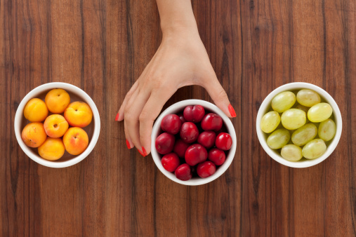 Three bowls with varieties of fruits and woman's hand holding the middle one