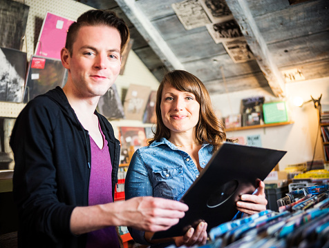 A cute couple in their 30s having fun shopping for vinyl records in an old school vintage record store.