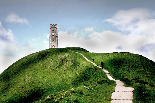 Glastonbury Tor rises up from the Somerset Levels in the West Country. Legends say that it has connections with the stories of King Arthur, the Wizard Merlin and the possible location of Avalon. There is an ancient stone tower at the top of this magnificent mound. There are shadowy figures in the middle distance, trudging up the long path to the summit.