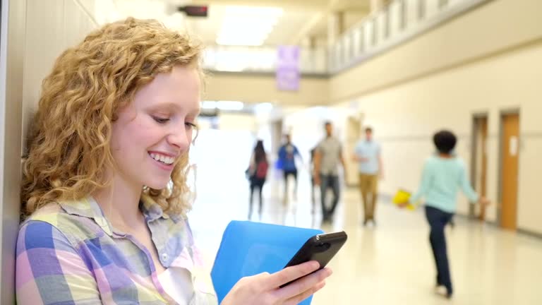 Teen girl laughing while she texts on smart phone in high school hallway before class