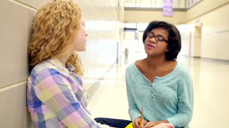 Teen girls sitting in hallway of high school and talking after class