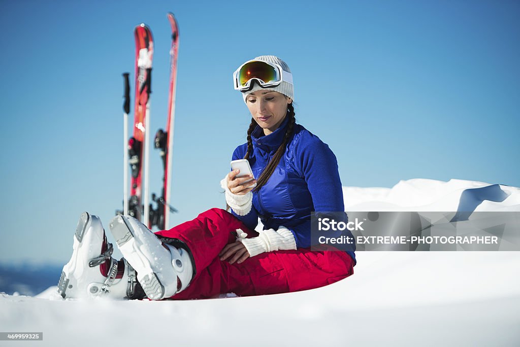 Snow activities Woman on the mountain sitting in the snow and checking mobile messages after ski activities. Alpine Skiing Stock Photo