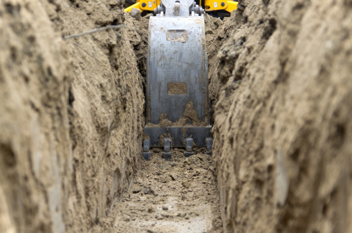 Low level view of a backhoe bucket as it digs a trench to bury an electrical power line.