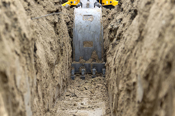 Digging Power Line Trench Low level view of a backhoe bucket as it digs a trench to bury an electrical power line. digging stock pictures, royalty-free photos & images