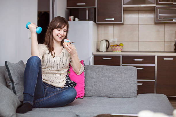 Smiling woman lying on sofa with cupcake and a hantel Smiling woman lying on sofa with cupcake and a hantel hantel stock pictures, royalty-free photos & images