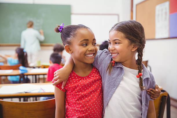 Cute pupils smiling at camera in classroom Cute pupils smiling at camera in classroom in slow motion arm around stock pictures, royalty-free photos & images