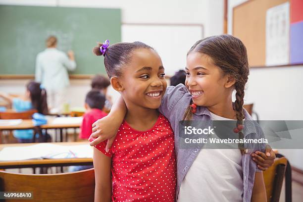 Cute Pupils Smiling At Camera In Classroom Stock Photo - Download Image Now - Child, Arm Around, Education