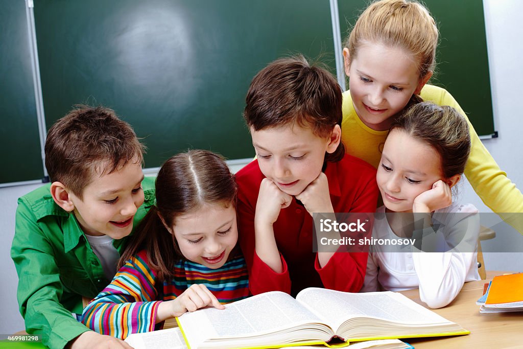 Reading lesson Portrait of friendly group reading book in classroom 2015 Stock Photo