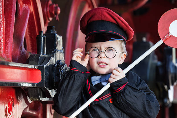 Upset Little Railroad Conductor Portrait of a cute little child boy with annoyed facial expression as nostalgic railroad conductor and metal-rimmed glasses, cap and signaling disk transport conductor stock pictures, royalty-free photos & images