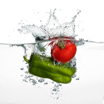 Closeup of fresh tomato and Pepper falling into clear water with big splash isolated on white background. Healthy eating