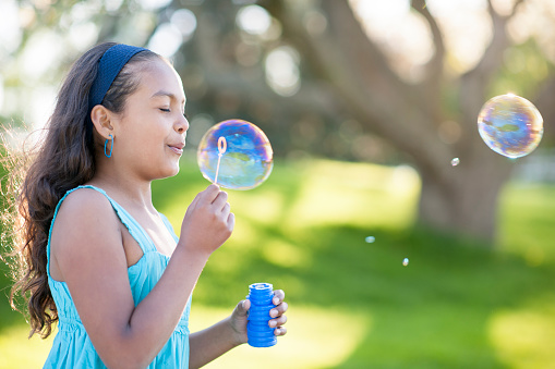 Little girl at the park with a sunlight effect, blowing bubbles from a bubble wand.