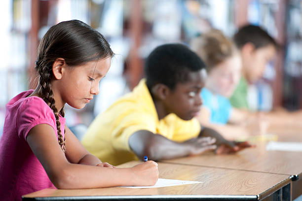 Group of Children in Class Elementary school students taking a test, or doing schoolwork at their desks in a classroom. report card stock pictures, royalty-free photos & images