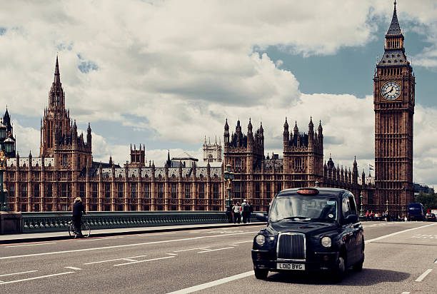 London, UK - May 6, 2014: An iconic taxi cab drives past Big Ben and over the Westminster Bridge