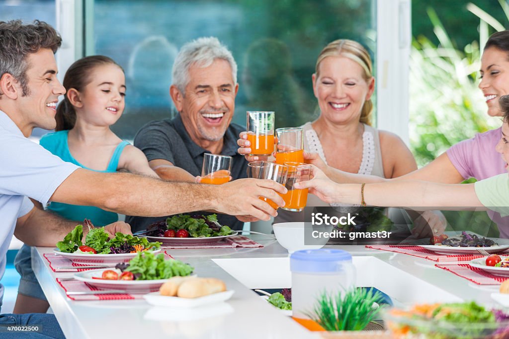 A big family celebrating at their meal multy-generation generation family, parents, children and grandparents, drink orange juice toast happy smile lunch dinner sitting at table, home Family Stock Photo