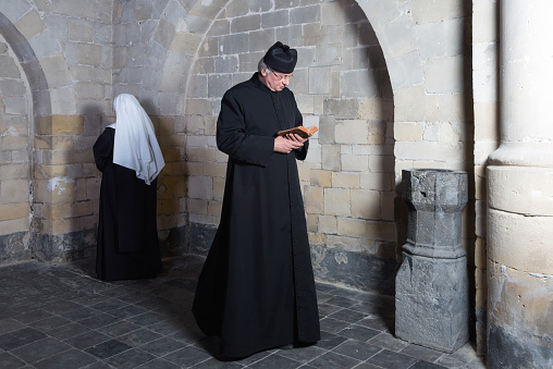 Priest passing a young nun along the walls of a medieval abbey