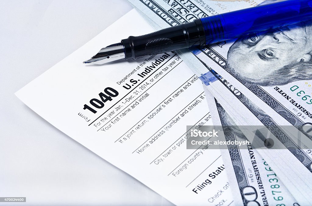 Income Tax Form Tax form 1040 on a gray background, blue pen, and 100 dollar bills 1040 Tax Form Stock Photo