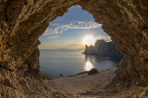 View from a small grotto on an evening sun setting behind the coastal cliffs. Crimea.