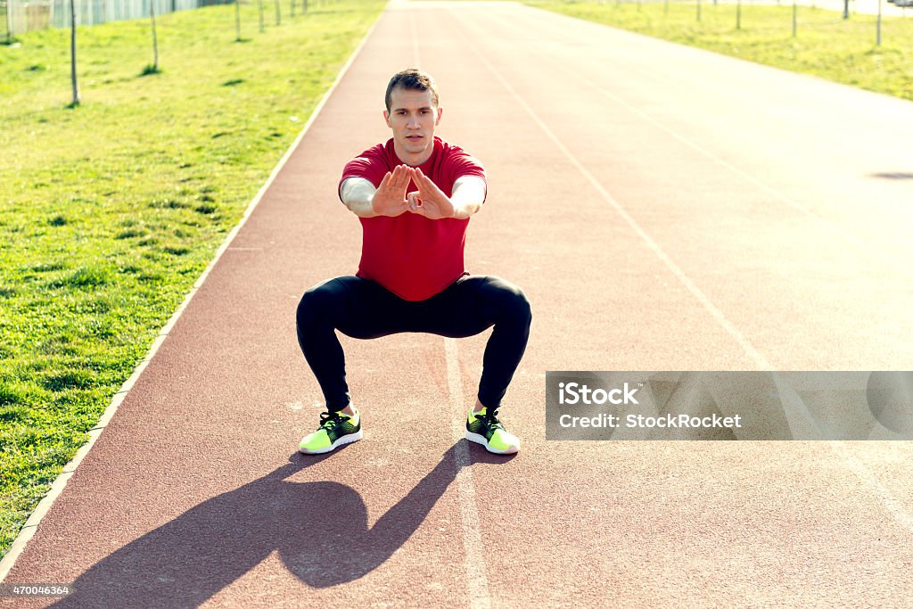 Male athlete doing squats on track Young man working out outside 2015 Stock Photo