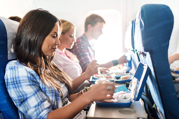 Passengers having lunch while traveling by airplane. Group of people travelling by airplane. Focus is on foreground, on young woman preparing herself for eating lunch. economy class stock pictures, royalty-free photos & images