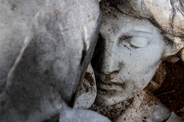 Face of a woman statue behind a rock stock photo