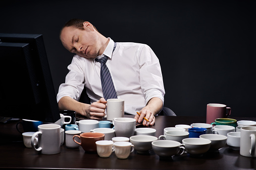 Exhausted businessman sleeping at table, surrounded with many empty coffee cups