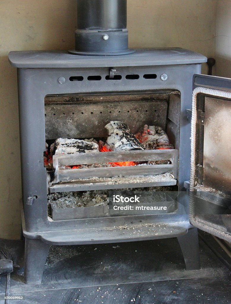 Image of cast-iron multi-fuel stove burning wood, fire / flames, open-door Photo showing a small cast iron woodburner, which has been pictured with its door open to reveal the logs, ash and warming fire burning inside.  Metal wood burning stoves are often referred to as multi-fuel stoves, since they are able to burn either wood or alternatively, a smokeless fuel, such as coke, coal or charcoal options. Ash Stock Photo