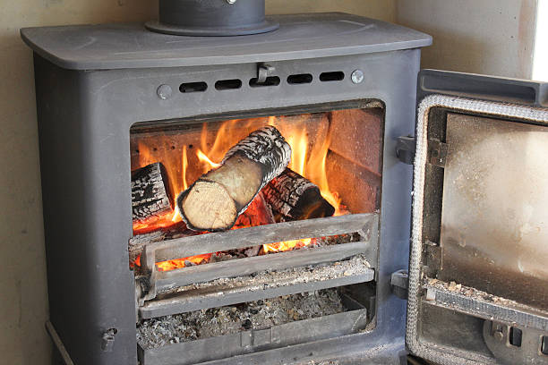 Image of roaring fire / flames, wood-burning multi-fuel stove / fireplace, door-open Photo showing a traditional cast iron woodburner, pictured with its door open to reveal the logs and roaring fire burning inside, with big orange flames. Metal wood burning stoves are often referred to as multi-fuel stoves, since they are able to burn either wood or alternatively, a smokeless fuel, such as coke, coal or charcoal options. back boiler wood burner stock pictures, royalty-free photos & images